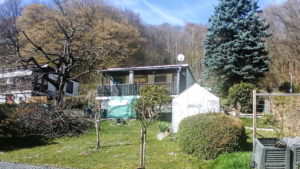 Bild des g.nr61 mit gr Kirschbaum, unterkeltertem Bungalow, Gewächshaus u. Wald im Hintergrund